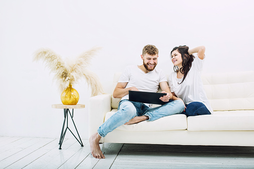 Young beautiful and happy couple man and woman at home with tablet in white interior