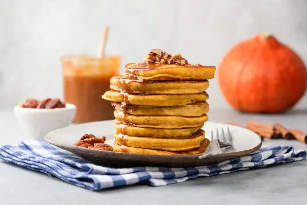 Stack of pumpkin pancakes with caramel sauce and pecan nuts on a plate, closeup view. Tasty autumn comfort food