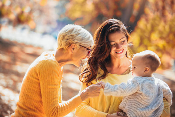 abuela y madre sonriendo en el bebé en el parque de otoño. - outdoors offspring women fall fotografías e imágenes de stock