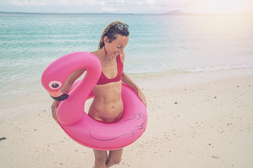 Young woman walking on idyllic beach with inflatable flamingo in the Islands of Thailand. People travel destinations fun and cool attitude concept