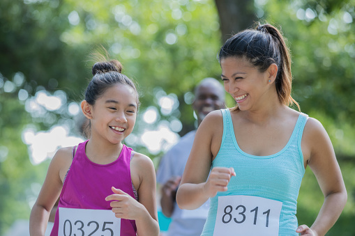 Mid adult Filipino woman and her elementary age daughter are running together in a charity marathon race event. Mother is encouraging daughter to keep going.