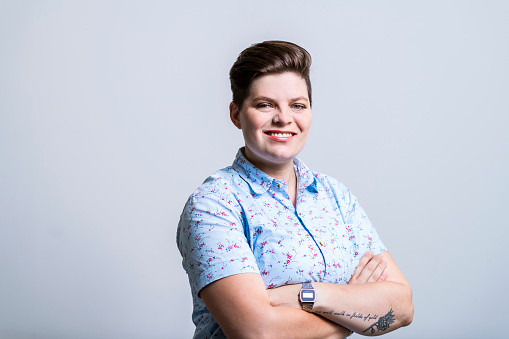 Portrait of confident creative businesswoman and entrepreneur against gray background. Female entrepreneur is smiling while standing with arms crossed. She is wearing patterned shirt.
