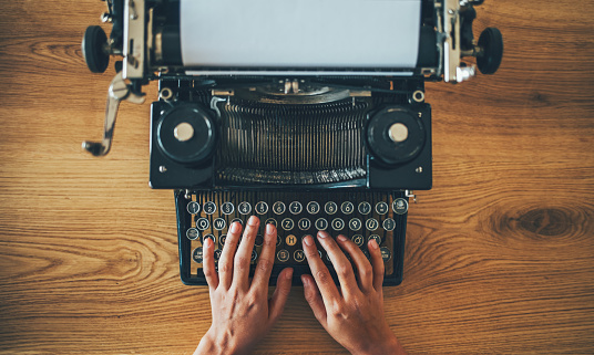 High angle view of writer's hands prints on vintage typewriter on wooden desk.