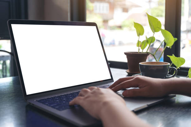 istock Mockup image of a woman's hands using and typing on laptop with blank white desktop screen with coffee cup on wooden table in cafe 1057475056