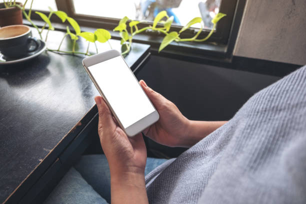 istock Mockup image of a woman's hands holding white mobile phone with blank desktop screen while sitting in cafe 1057475152