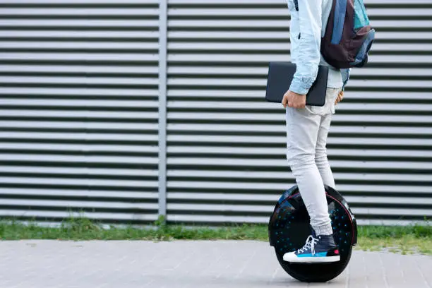 Modern young adult male businessman student freelancer with backpack and laptop riding on ecological electric transport futuristic eco electric unicycle scooter, balancing electric wheel. Eco planet.