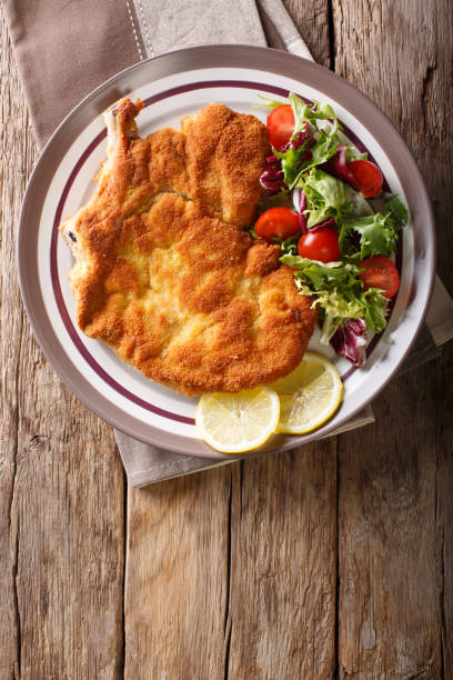 veal milanese with lemon and fresh salad of tomatoes and lettuce close-up. vertical top view - milanese imagens e fotografias de stock