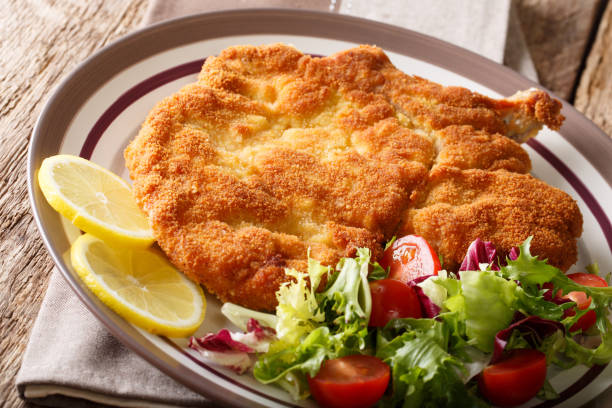 Traditional Italian veal Milanese with lemon and fresh vegetable salad close-up. horizontal Traditional Italian veal Milanese with lemon and fresh vegetable salad close-up on a plate. horizontal scaloppini stock pictures, royalty-free photos & images
