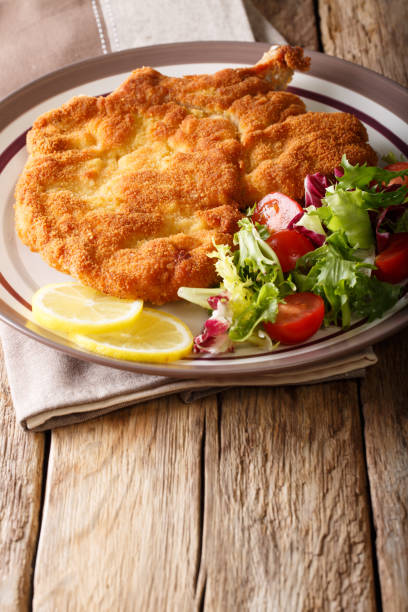 Fried veal cutlet Milanese with lemon and fresh salad of tomatoes and lettuce close-up on a table. vertical Fried veal cutlet Milanese with lemon and fresh salad of tomatoes and lettuce close-up on a plate on a table. vertical scaloppini stock pictures, royalty-free photos & images