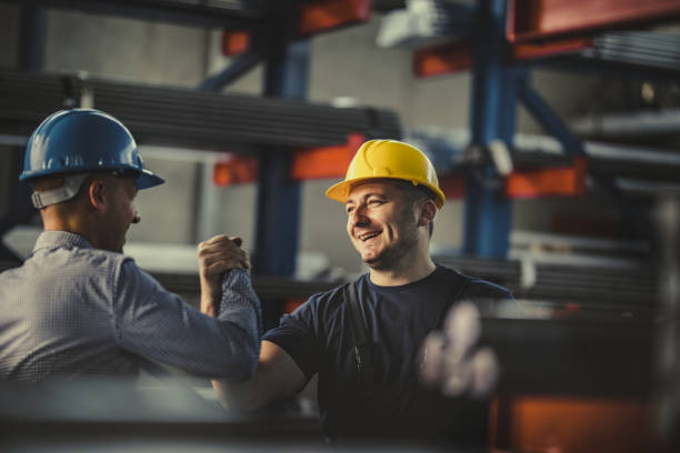 Young happy worker and manager giving each other manly greet at steel mill. Happy metal worker greeting his manager in aluminum mill. working class stock pictures, royalty-free photos & images