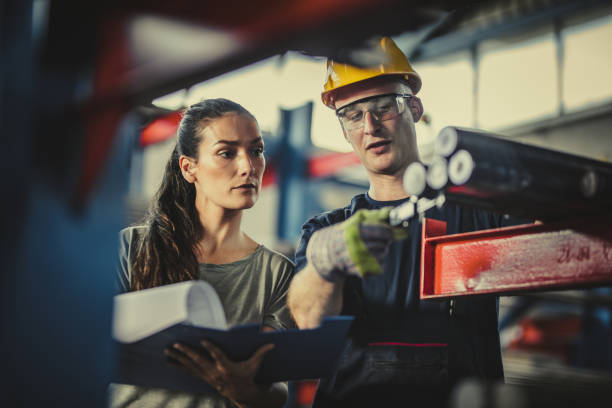 Female manager and manual worker analyzing steel in industrial building. Young female foreman and her manual worker working on paperwork and steel in aluminum mill. metallurgy stock pictures, royalty-free photos & images