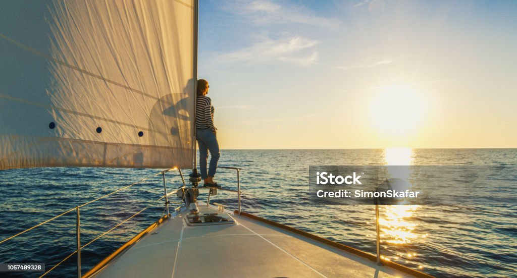 Woman staying on edge of prow, Croatia Woman staying on edge of prow and looking at sunset, Croatia Sailboat Stock Photo