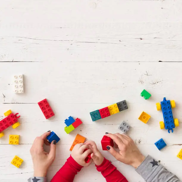 Photo of Top view on child's and mother's hands playing with colorful plastic bricks, toys and building from them. Learning by playing.