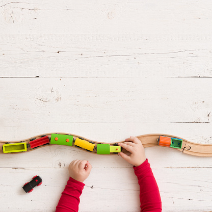 Vista superior en trenes de madera de juguete en ferrocarril en el fondo de la tabla de madera blanca. Manos del niño jugando con juguetes educativos. photo