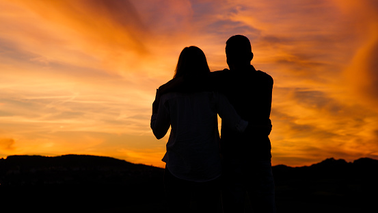 Silhouette of couple sitting under moody sky, hugging each other