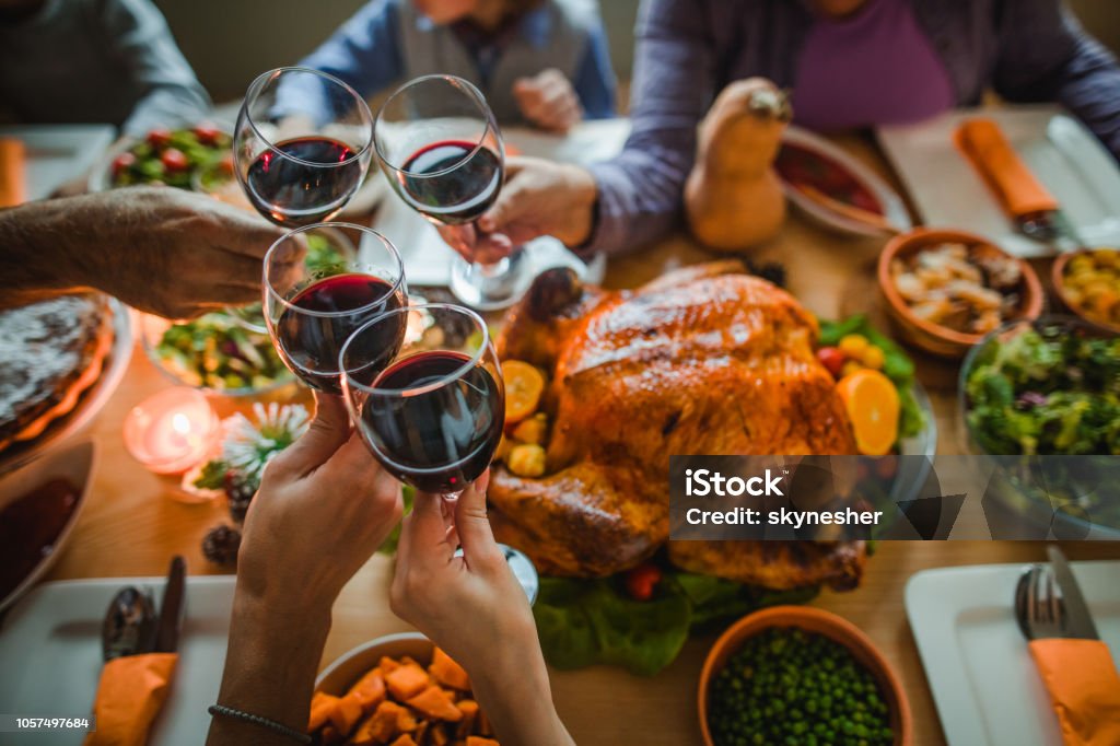 Cheers to this great Thanksgiving dinner! Group of unrecognizable people toasting with wine during Thanksgiving dinner at dining table. Thanksgiving - Holiday Stock Photo