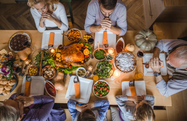 acima vista da família estendida dizendo graça antes do jantar de ação de graças. - family thanksgiving dinner praying - fotografias e filmes do acervo