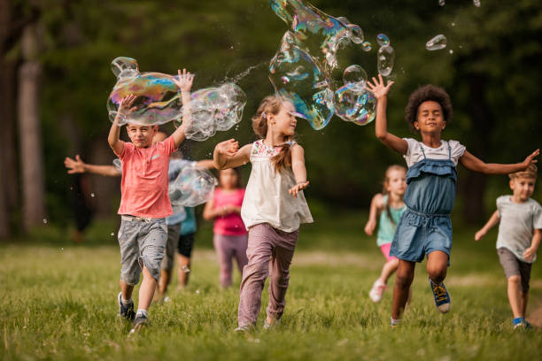 istock Carefree kids having fun while running through rainbow bubbles in the park. 1057502568