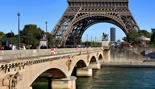 Paris, France, September 30, 2015: People cross the Bridge d'Iéna over the Seine River under the Eiffel Tower in Paris. In the background Montparnasse skyscraper.