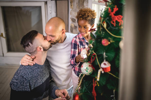 istock Gay couple kissing while decorating a tree with their adopted daughter 1057523926