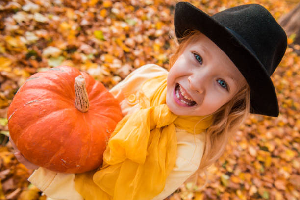 Little beautiful blond girl with big pumpkin in autumn background stock photo