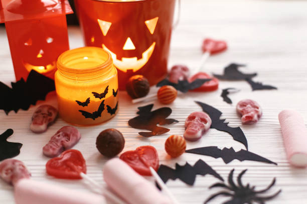 istock Halloween Jack o Lantern, candle light, holiday candy, bats, spiders, skulls on white rustic wooden background. Trick or treat. Halloween background. Season's greeting card 1057539058