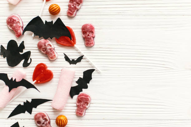 istock Halloween  flat lay. Holiday candy with bats, spiders, ghosts, skulls top view on white rustic wooden background. Trick or treat. Halloween background. Season's greeting card mockup 1057539062