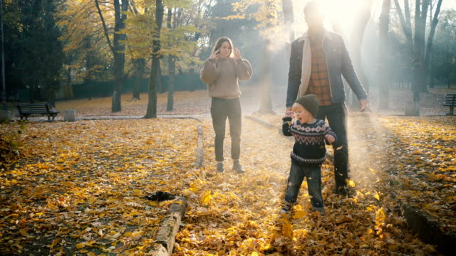 Young Caucasian mother and father  playing with little son in park in autumn