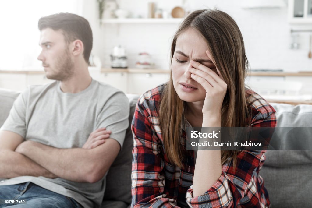 Couple conflict. Stressed crying female sitting on couch with abusive husband after quarrel, ready to divorce Couple - Relationship Stock Photo
