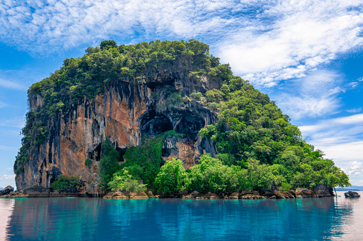 The scene from the Andaman Sea, looking towards the famous destination ‘skull island’ i.e. Ko Pi, Ko Lanta, Krabi, Thailand.  These stunning limestone Karst Islands rise up from the Andaman Sea.  The weathered rocks have crumbled to form caves that resemble a human skull.