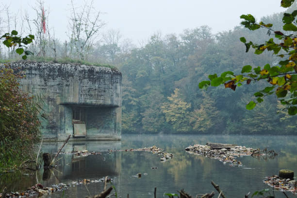 A world war two bunker built on the river rhine in Switzerland during misty morning hours in autumn. A beautifully colored forest in the background.