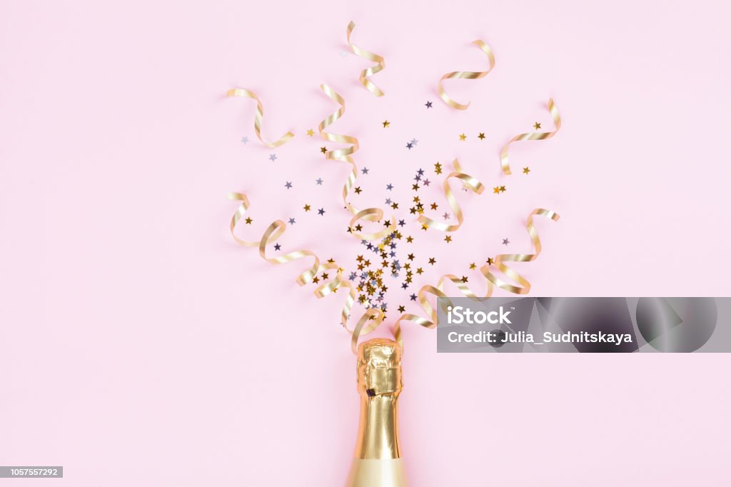 Champagne bottle with confetti stars and party streamers on pink background. Christmas, birthday or wedding concept. Flat lay. Champagne bottle with confetti stars and party streamers on pink background. Christmas, birthday or wedding concept. Flat lay style. Celebration Stock Photo
