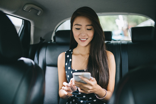 Young student sitting on the backseat of a taxi. She's checking her smartphone for the street name.