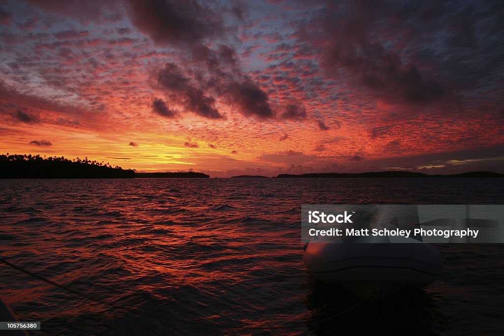 Dinghy in the Sunset The sun setting over the islands of Vava'u, Tonga, with an outboard boat floating in the sea in the foreground. Affectionate Stock Photo