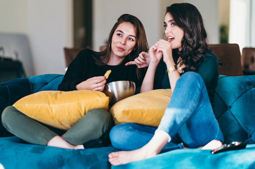 Two young women friends are watching TV together.