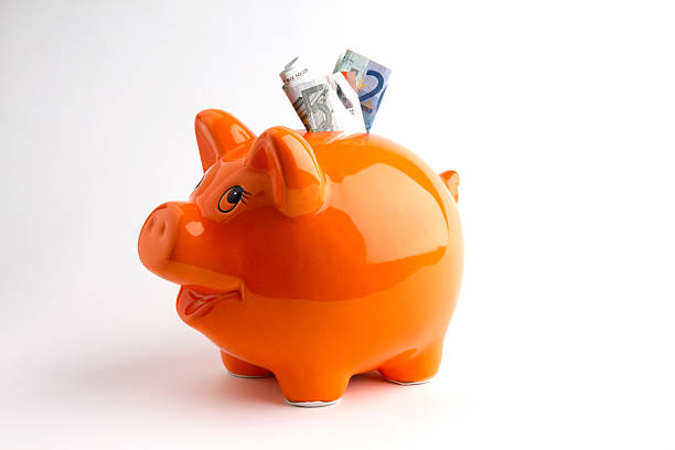 Orange piggy bank with bills coming out of the top Piggibank tabletop with soft shadow. five euro banknote photos stock pictures, royalty-free photos & images
