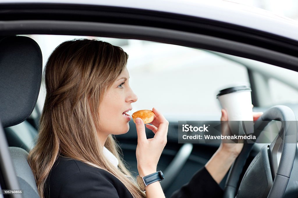 Charming businesswoman eating and holding a drinking cup while driving Charming businesswoman eating and holding a drinking cup while driving to work Driving Stock Photo