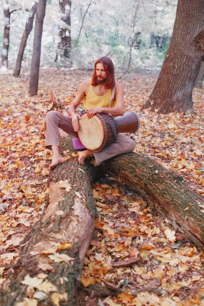 Hippie man playing djembe drum in autumn forest.