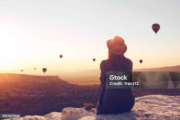View From The Back Of A Girl In A Hat Sits On A Hill And Looks At Air Balloons Stock Photo - Download Image Now