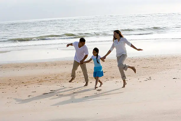 Photo of Hispanic family holding hands skipping on beach