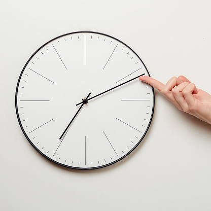 Woman hand stop time on round clock, female finger takes minute arrow of the clock back, time management and deadline concept