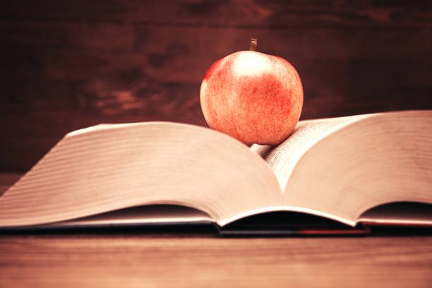 istock Reading book open on wooden background and red apple. 1057662182