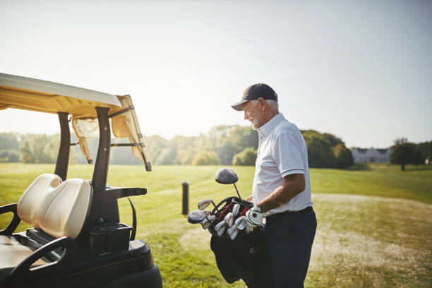 カートにゴルフ クラブかばんを置く年配の男性 - golf cart golf bag horizontal outdoors ストックフォトと画像