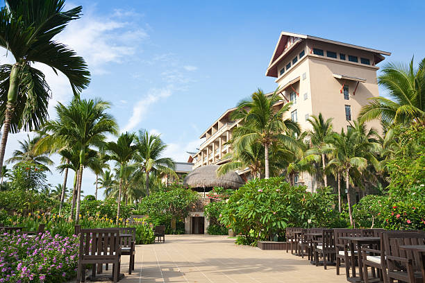 Luxury beach cabanas with wooden exteriors, white curtains, and sun loungers, surrounded by greenery along a wooden pathway in a tropical resort setting