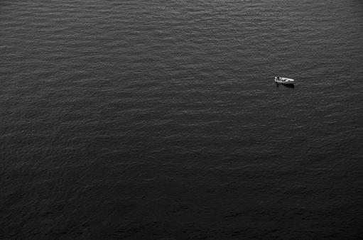 A black and white picture of a small fishing boat alone in the vastness of the sea.