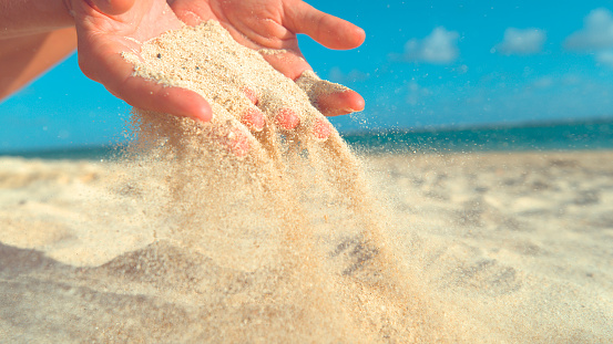 Sand running through hands on beach.