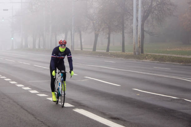 Cyclist passing the empty city street on foggy morning stock photo