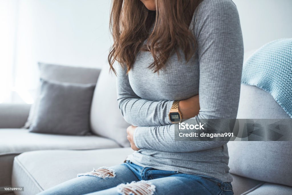 Woman lying on sofa looking sick in the living room Woman lying on sofa looking sick in the living room. Beautiful young woman lying on bed and holding hands on her stomach. Woman having painful stomachache on bed, Menstrual period Stomachache Stock Photo