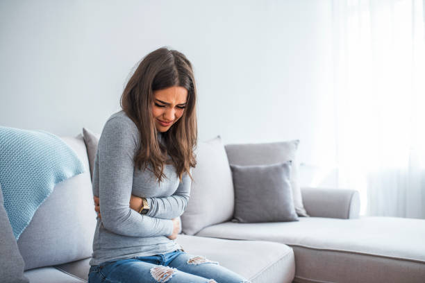 Woman having painful stomachache on bed Woman lying on sofa looking sick in the living room. Beautiful young woman lying on bed and holding hands on her stomach. Woman having painful stomachache on bed, Menstrual period diarrhea photos stock pictures, royalty-free photos & images