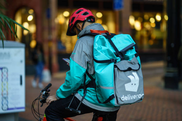 Delivery food courier guy from Deliveroo checking order via mobile phone. Coventry, UK - October 18, 2018 - Delivery food courier guy from Deliveroo checking order via mobile phone. west midlands photos stock pictures, royalty-free photos & images